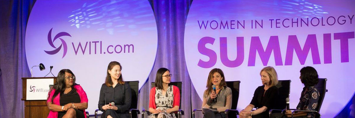 A panel of women discuss in front of a pair of printed Full Moons at the Women in Technology Summit. The Full Moon on the right has the name of the summit printed on it; the left Full Moon has WITI.com printed on it with the WITI logo.