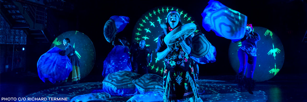 A dancer with a drum performs with IBEX puppetry in front of Full Moons which are both printed on and projected onto, for the performance Ajijaak on Turtle Island. Photo courtesy of Richard Termine.